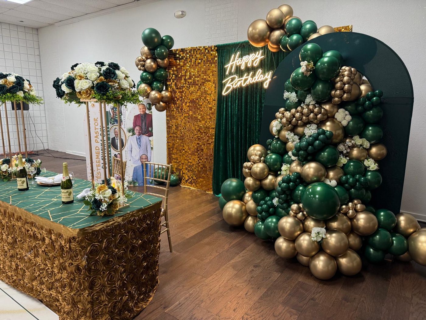 A reception set-up with a gold sequin drape, an emerald arch panel, a rose-textured gold table and a green and gold balloon cascade.